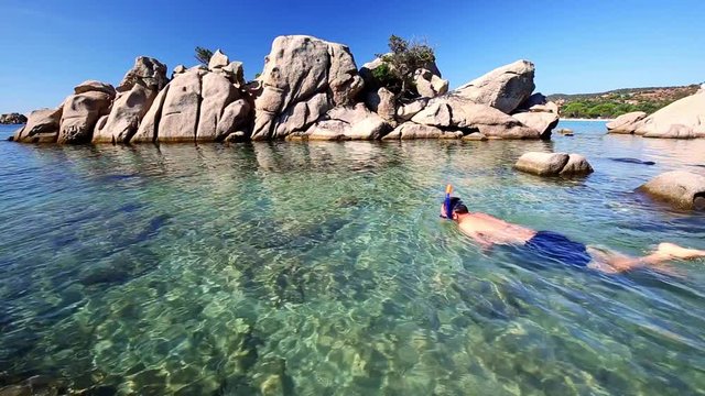 Young attractive man snorkeling in green lagoon near famous pine tree on Palombaggia sandy beach on the south part of Corsica, France, Europe
