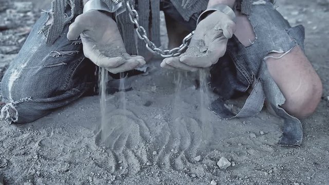 a prisoner in chains on his knees touching the dusty ground
