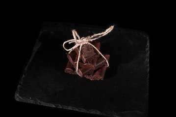 Stack of black pore chocolate on a black background, bounded with thread