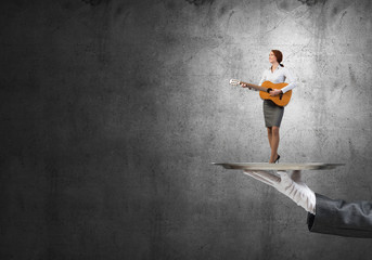 Fototapeta na wymiar Attractive businesswoman on metal tray playing acoustic guitar against concrete wall background
