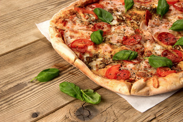 Hot and delicious pizza with salami tomatoes cheese and mushrooms ready to eat  on a wooden background.