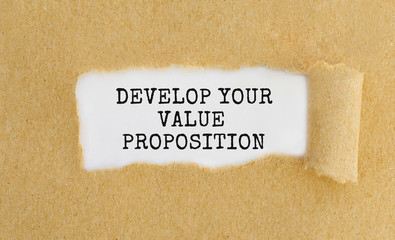 Text Develop Your Value Proposition appearing behind ripped brown paper