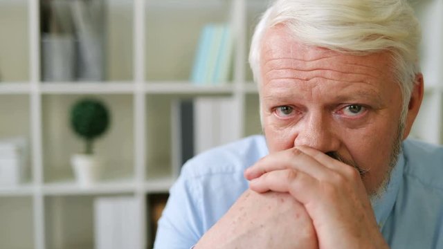 Portrait of caucasian midle aged conceived man proping his faces by hands at office background. Indoor. Close up