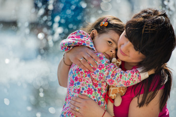 Obraz premium A small charming girl hugs her mother in the park near the fountain. Mothers Day.