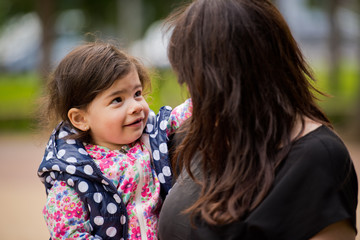 A small daughter in her mother's arms looks at her with a questioning glance. Mothers Day.