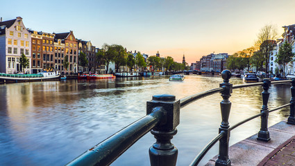 The most famous canals and embankments of Amsterdam city during sunset. General view of the cityscape and traditional Netherlands architecture. - obrazy, fototapety, plakaty