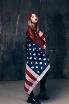 Girl is covered by american flag on dark background. Patriot, national event celebration, pride, usa citizen concept