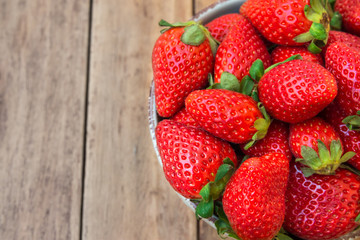 Ripe organic strawberries in ceramic bowl on plank wood background, close up, healthy food, cleansing concept, top view