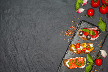 Appetizer bruschetta with pear, cheese, salmon, bacon, tomatoes on black concrete table. Top view. Free space.Delicious snacks, sandwiches, crostini, antipasti on party or picnic time. 
