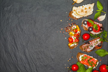 Appetizer bruschetta with pear, cheese, salmon, bacon, tomatoes on black concrete table. Top view. Free space.Delicious snacks, sandwiches, crostini, antipasti on party or picnic time. 