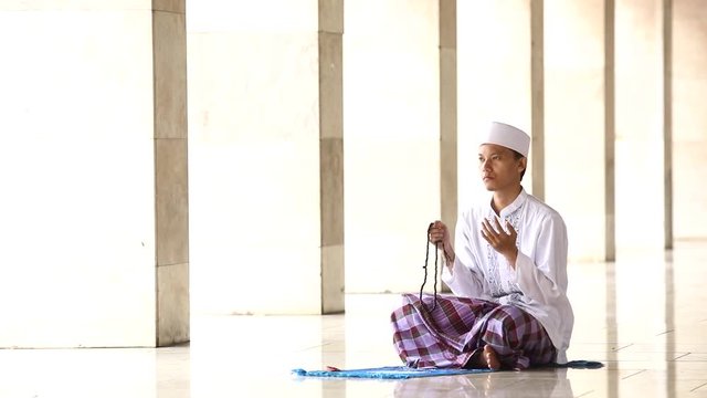  
Video footage of Asian muslim man sitting in the mosque, praying to the GOD while holding a praying beads, raising hands, and saying the praying words
