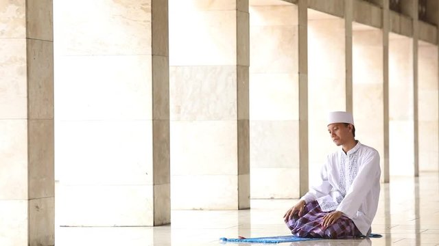  
Young religious muslim person praying in the mosque with final poses of prostration, sitting, and greeting or taslim
