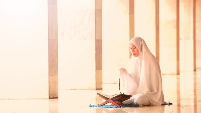  
Religious muslim woman doing dhikr with a praying beads while wearing prayer veil after reading Quran in the mosque
