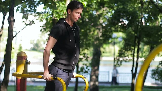 Young sportsman pushing up at the parallel bars in sunny day. Street workout.