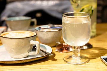 A Cup of coffee and a glass of water or lemonade stand on the table.