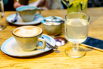 A Cup of coffee and a glass of water or lemonade stand on the table.