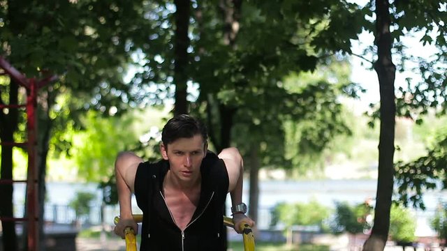 Young sportsman pushing up at the parallel bars in sunny day. Street workout.