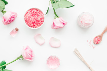 body treatment with rose flowers and cosmetic set white desk background top view