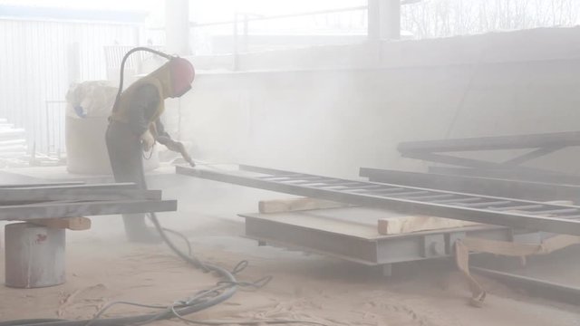 Worker sandblasting metal construction by sandblaster