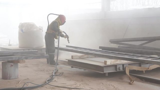 Worker sandblasting metal construction by sandblaster
