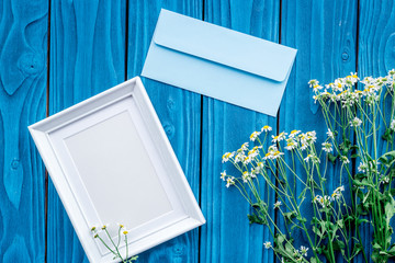 female desktop decoration with flowers and frame on blue wooden background top view mock-up
