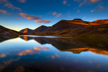 Fototapeta na wymiar Mountain lake at sunset of the day. Mountains against the background of the evening sky. The pond in the mountains. Stones in the water. Reflection in water.