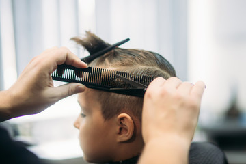 Fototapeta premium Little boy on a haircut in the barber sits on a chair.
