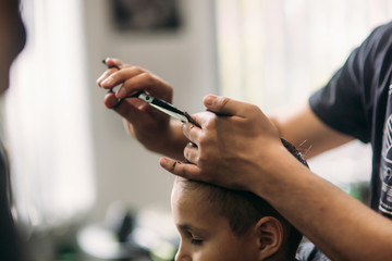 Fototapeta na wymiar Little Boy Getting Haircut By Barber While Sitting In Chair At Barbershop. 