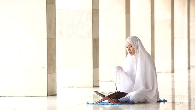  
Young religious muslim woman doing dhikr while holding a praying beads and wearing a prayer veil after reading Quran in the mosque
