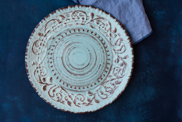 Blueish vintage empty plate, linen napkin on dark blue concrete table top, flat lay, menu template, copyspace, top view