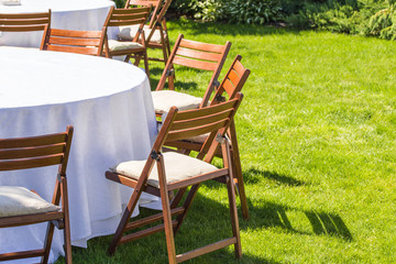 Round table covered with white cloth and chairs stand on a green lawn outdoors .