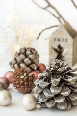 White Christmas decoration composition, big pine cones, scattered baubles, shiny star, wooden candle holder, dry tree branches in background, minimalist