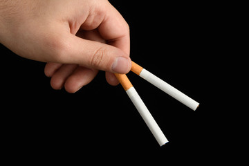 men's hand keeps in the fingers two cigarettes on black background