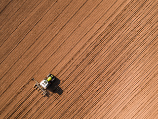 Obraz premium Aerial shot of a farmer seeding, sowing crops at field. Sowing is the process of planting seeds in the ground as part of the early spring time agricultural activities.