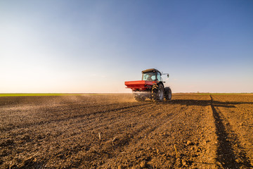 Fototapeta premium Farmer fertilizing arable land with nitrogen, phosphorus, potassium fertilizer