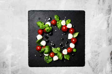 Caprese salad with mini mozzarella, green basil, cherry tomatoes, balsamic vinegar and olive oil, black stone tray, food background, top view