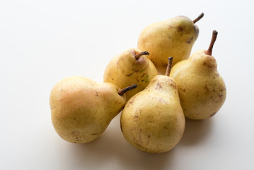 Close up view of natural looking yellow bartlett pears clustered together on white table (selective focus)