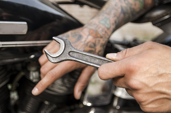 Tattooed hand of mechanic holding wrench and repairing bike 