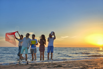 Group of happy young people is running on background of sunset beach and sea