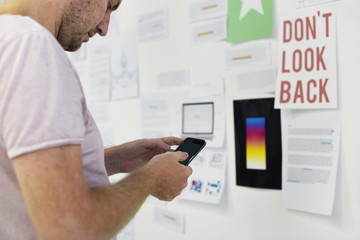 Man Standing infront of Startup Ideas Board Using Mobile Phone