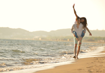A guy carrying a girl on his back, at the beach, outdoors