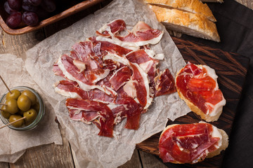 Jamon Iberico with white bread, olives on toothpicks and fruit on a wooden background. Top view