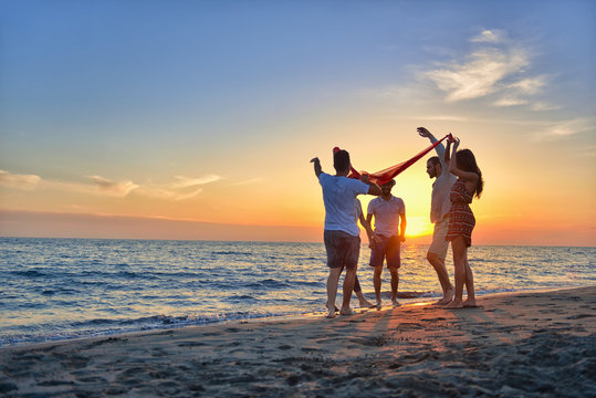 group of happy young people dancing at the beach on beautiful summer sunset