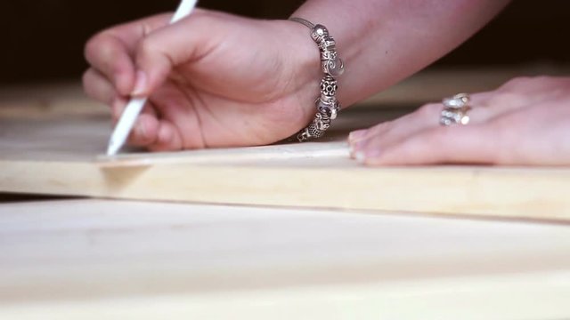 Woman traces along a wooden plank with a pen for a woodshop project - V1