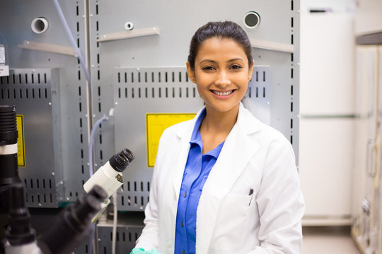 Closeup portrait, young smiling scientist in white lab coat standing by microscope. Isolated lab . Research and development.