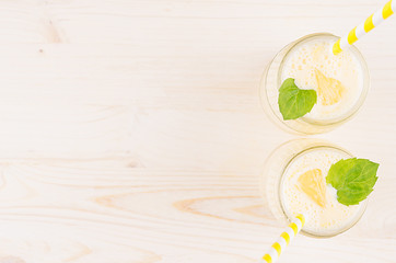 Freshly blended yellow lemon smoothie in glass jars with straw, mint leaf, top view. White wooden...