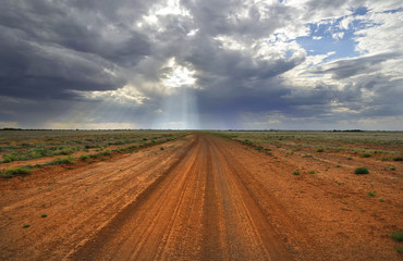 Fototapeta premium Country dirt road leads to sunbeams from sky.