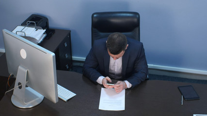 Bearded businessman using smartphone sitting at desk in office