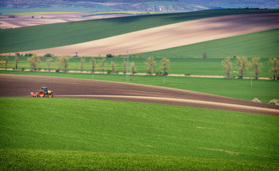 Agricultural landscape with tractor plowing a striped brown field in South Moravia at sunset, beautiful view on rolling hills, Czech Republic.