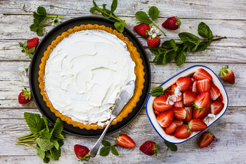 Delicious sponge cake with fresh strawberries and mascarpone on a wooden background.